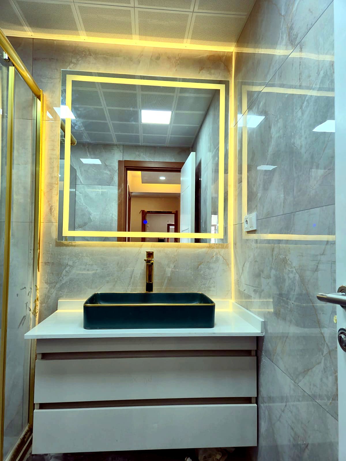 Altın çerçeveli ışıklı ayna ve koyu yeşil tezgah üstü lavabolu banyo