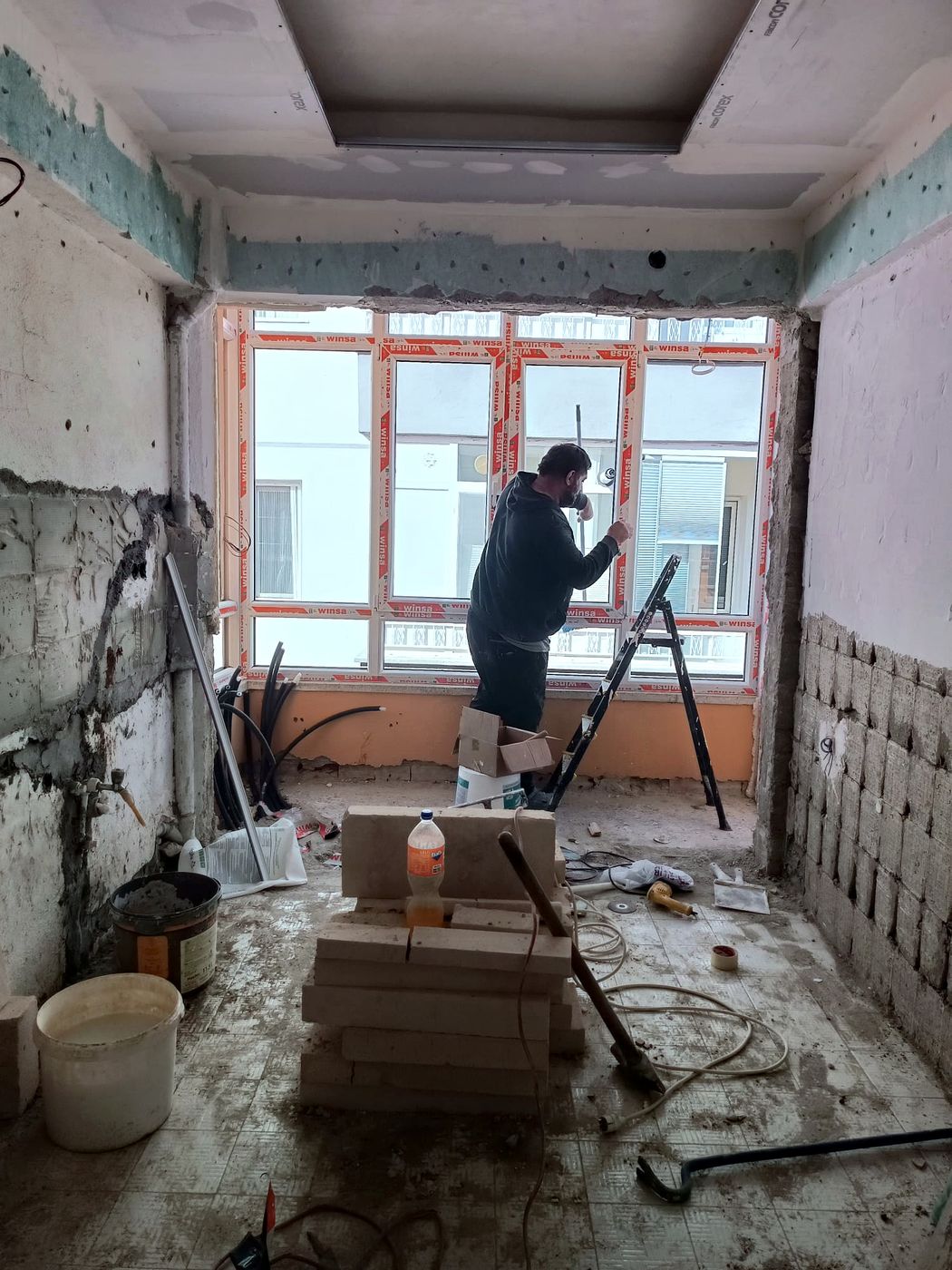 Pencere montajı yapan usta, sıvası dökülmüş oda